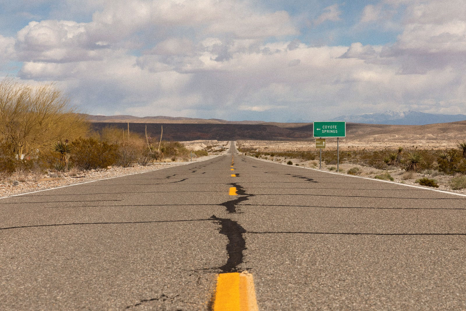 a green sign for coyote springs stands next to along stretch of desert highway