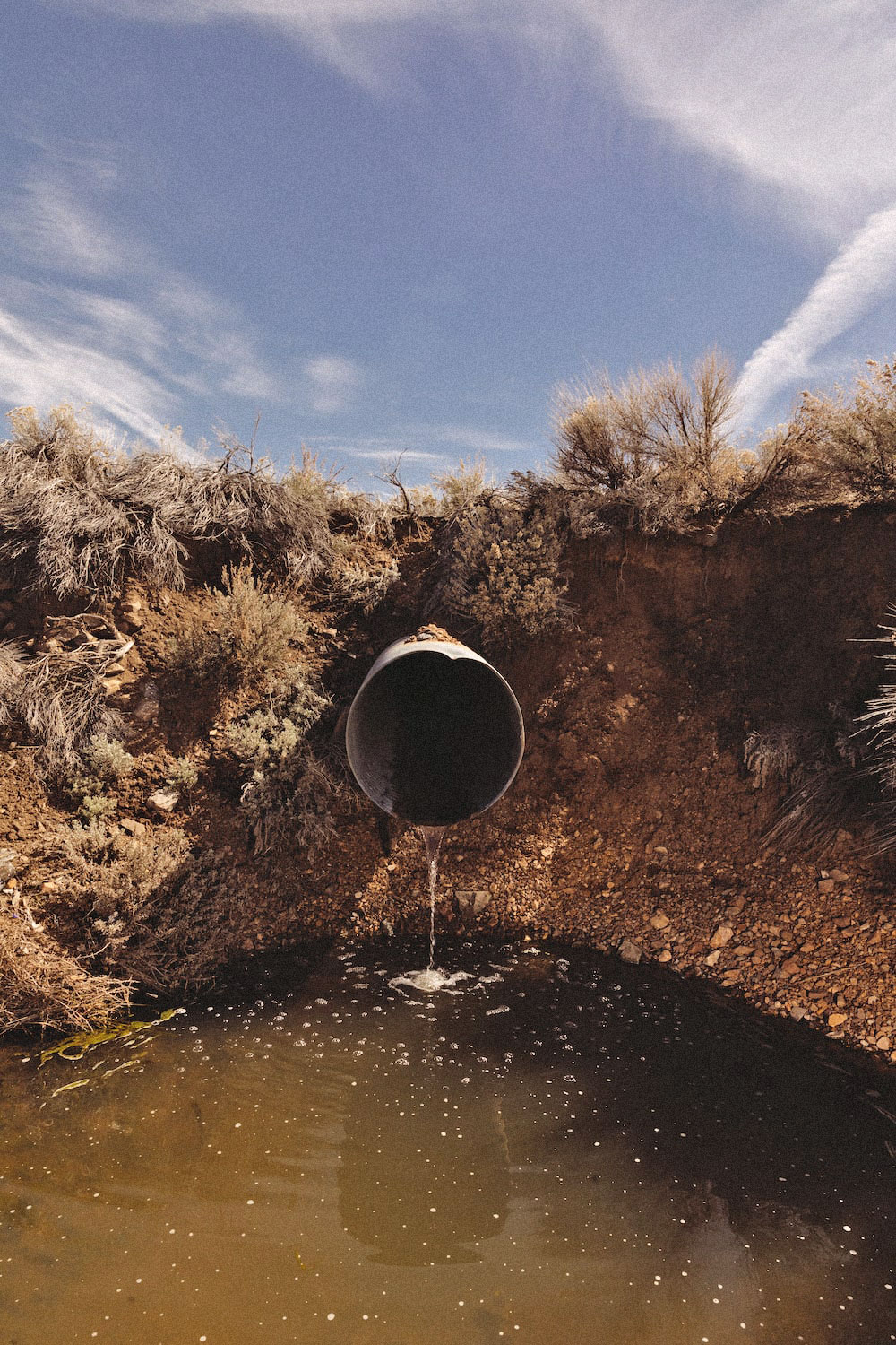 a pipe sticks out of the ground with water running through it draining into a puddle