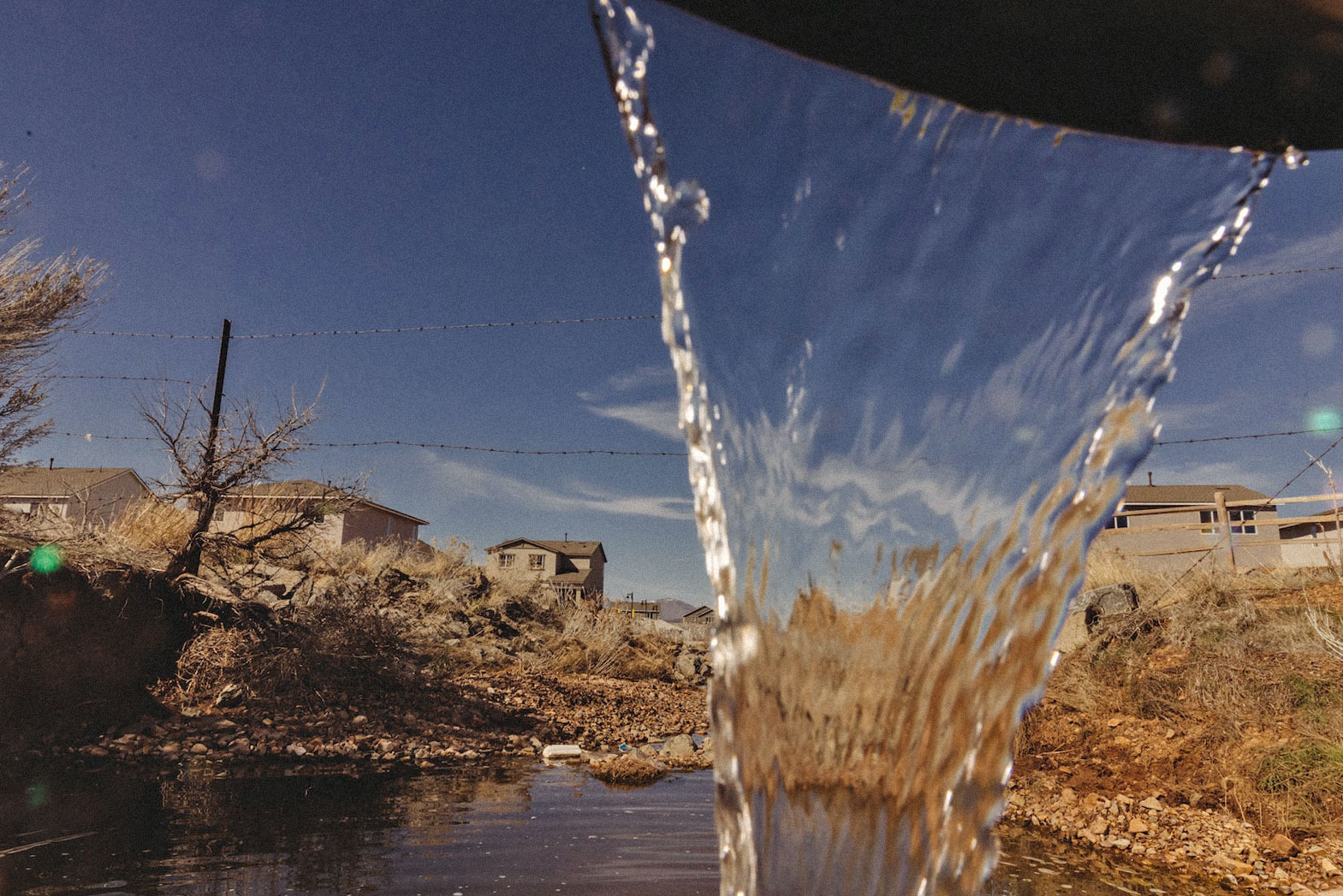 water flows out of a drainage pipe. Beyond the fall of water, houses and dry land.