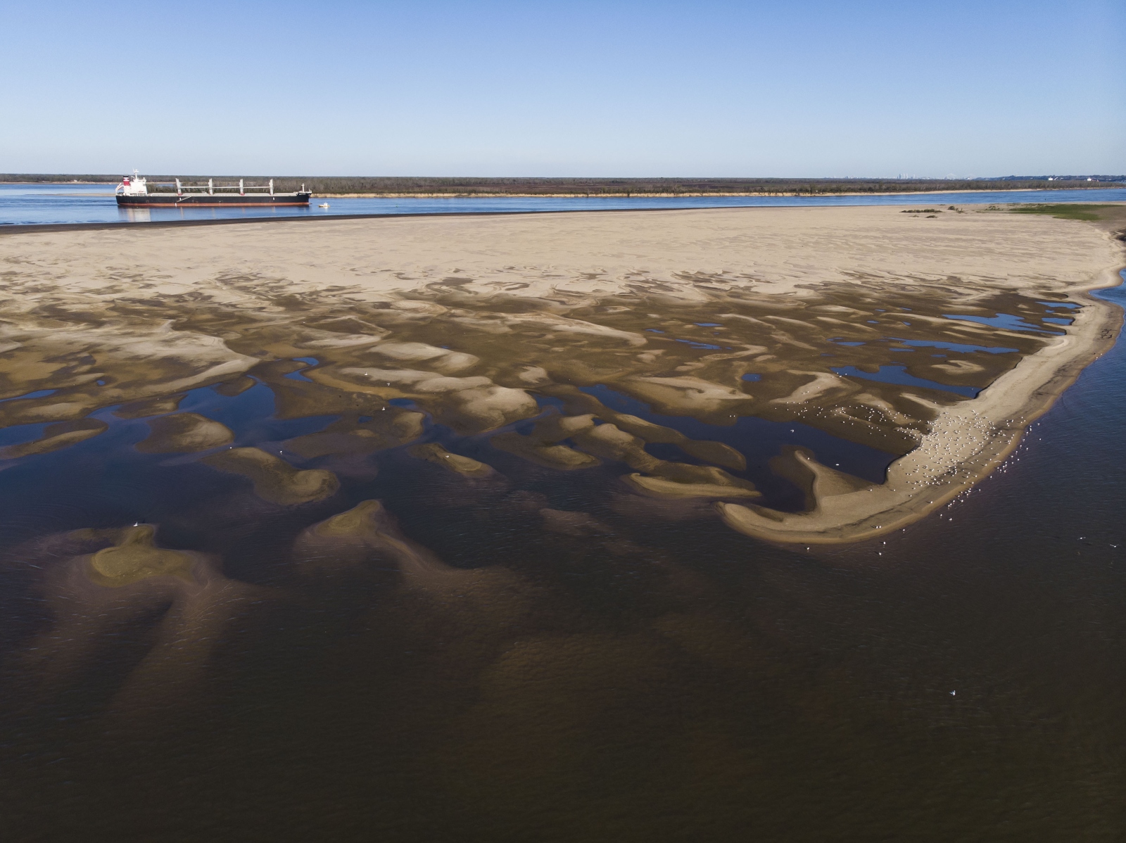 A view of a muddy sandbank with a tanker on a river in the background.