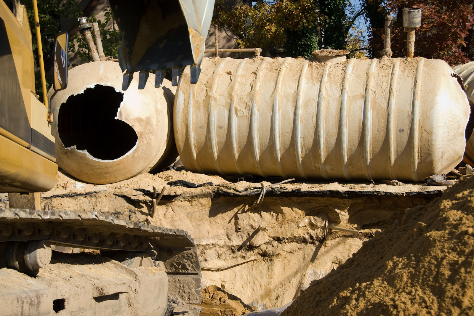 a large broken storage tank covered in dirt being held up by construction equipment