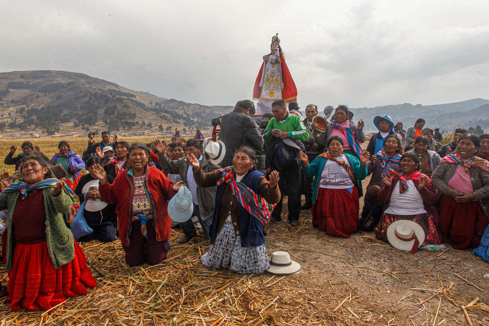 a group of people in colorful garments pray on their knees while holding a statue