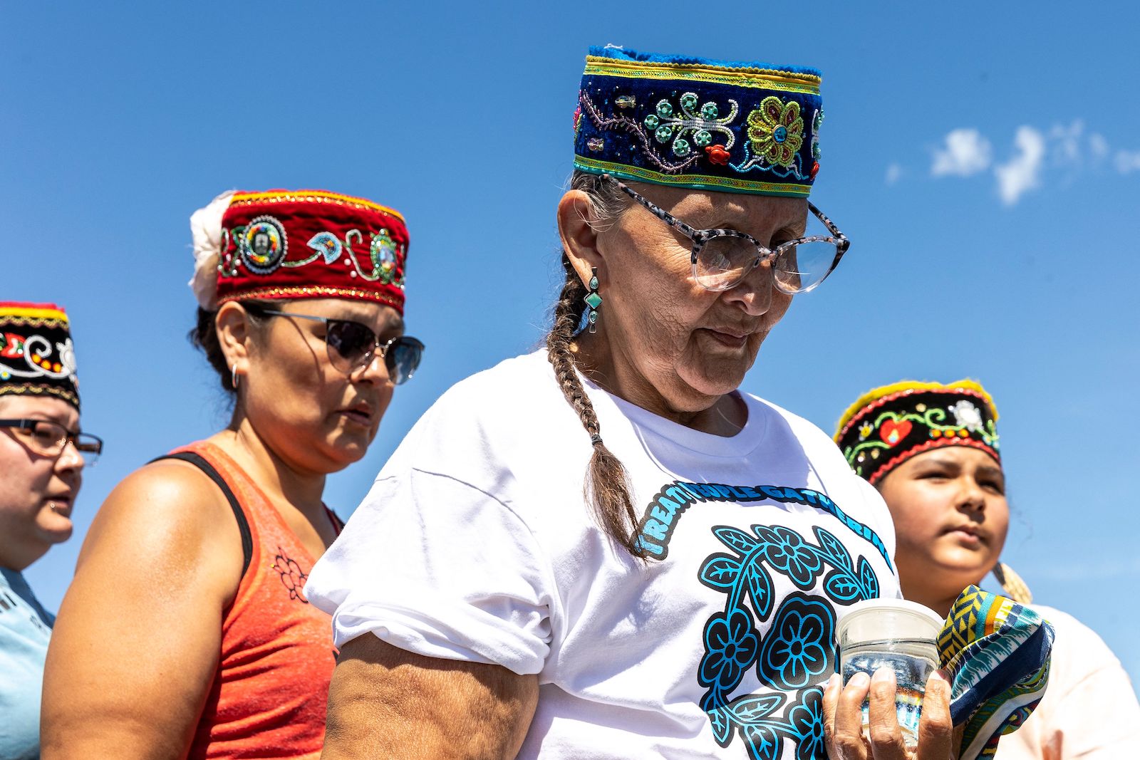 a group of people in embroidered hats pray over a glass of water