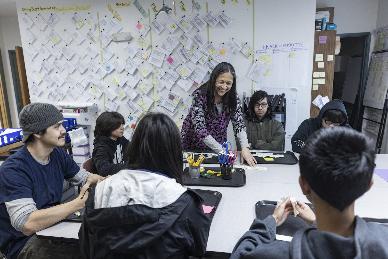 A teacher stands smiling at a table with six students sat around her