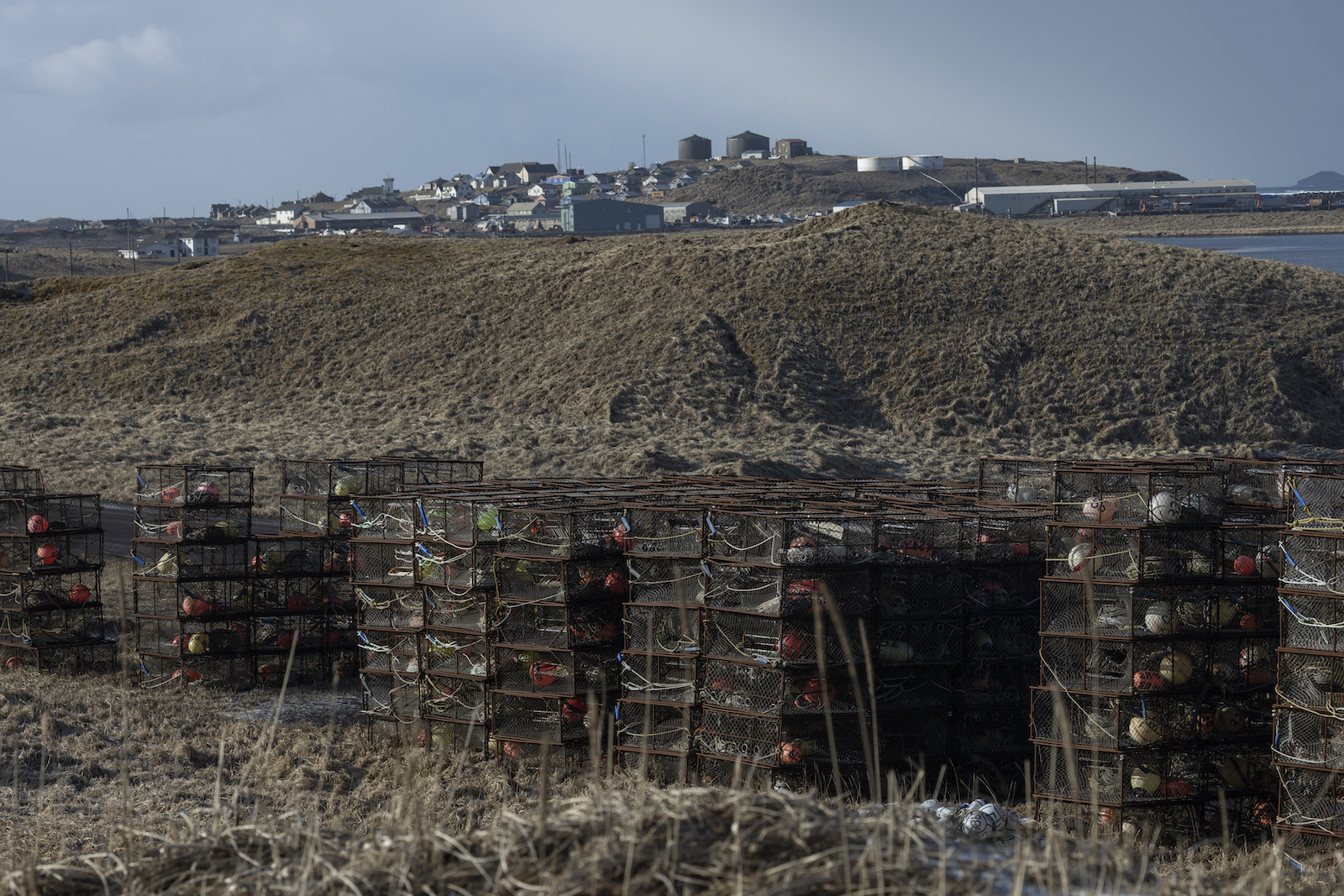 Empty crab pots are stacked, with the community of St. Paul visible in the background