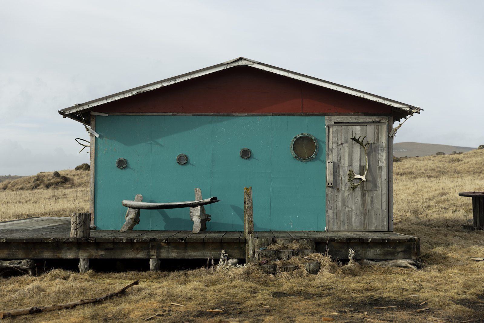 A small cabin with a turquoise facade and a wood door with an antler on it