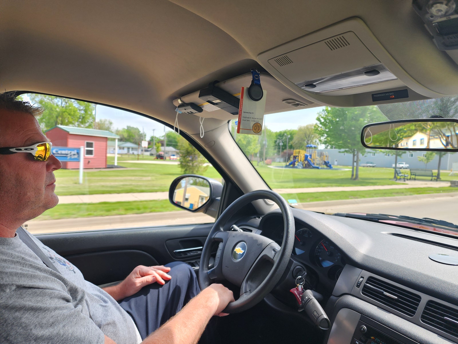 a man in sunglasses drives while a playground is seen out the window