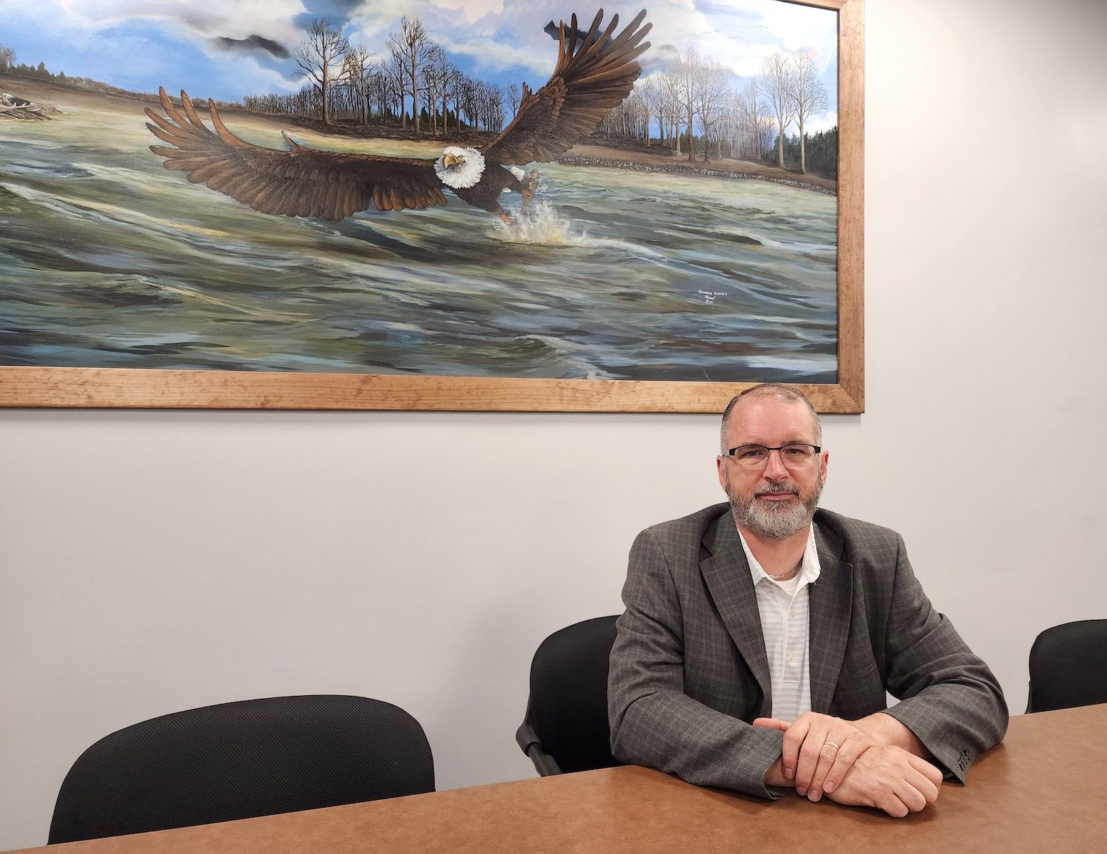 a man in a suit sits at a long table in front of an eagle painting