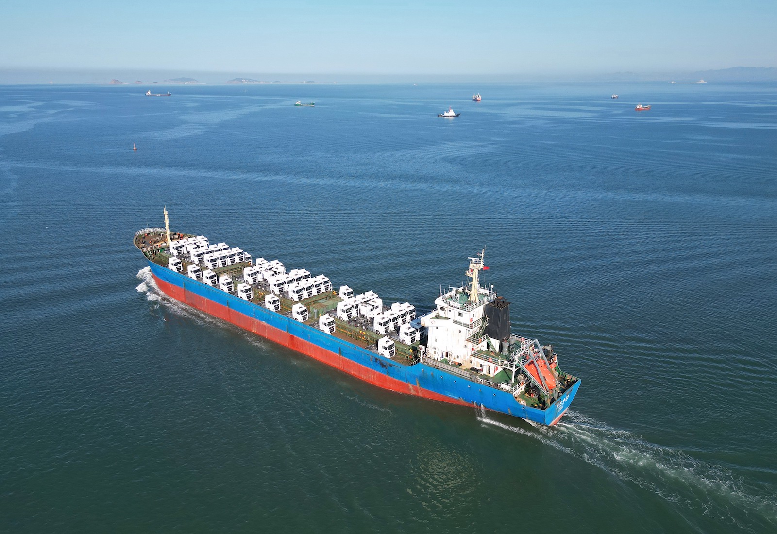 A ship loaded with heavy trucks leaves a port