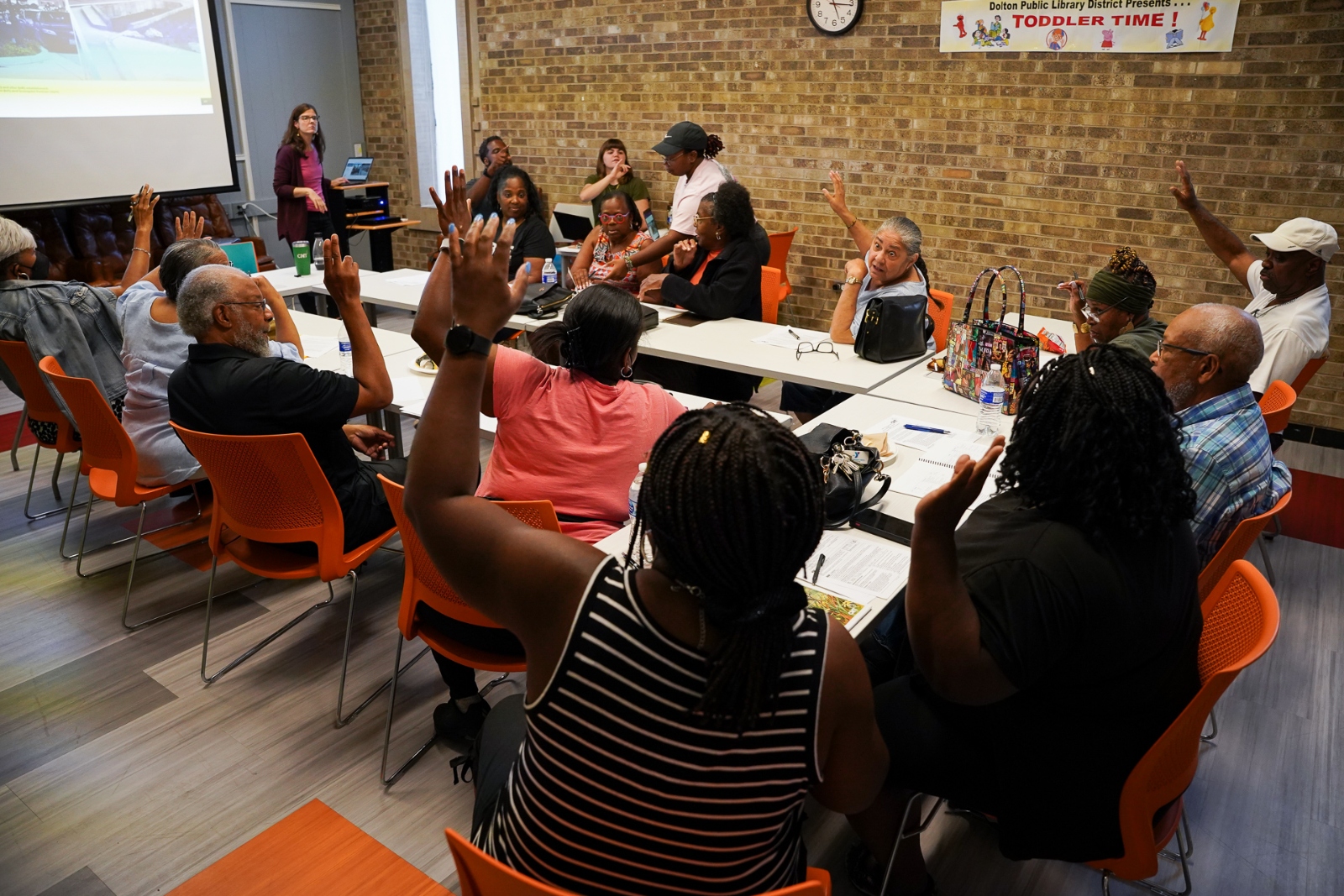 A group of people sit around a table with their hands raised.