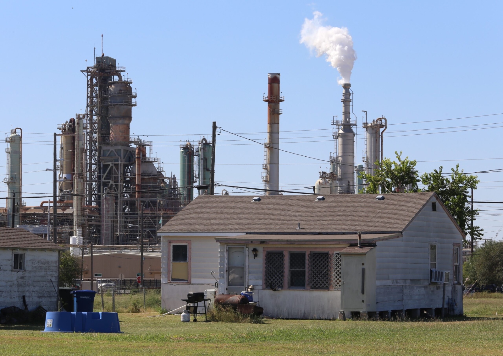 A small home sits in front of a factory with a smokestack belching smoke.