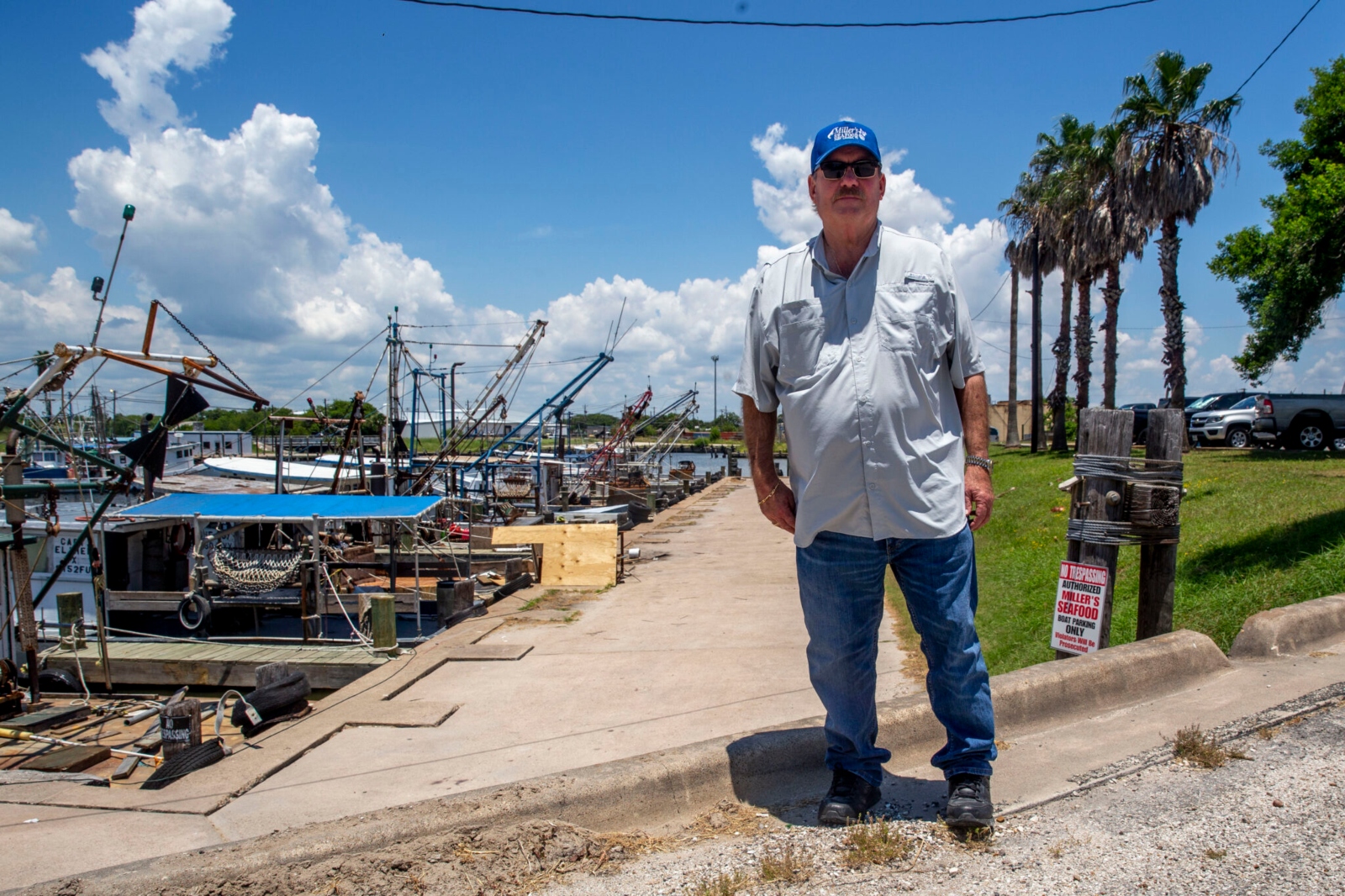 A man in a blue buttondown tee-shirt stands next to a port under blue skies.