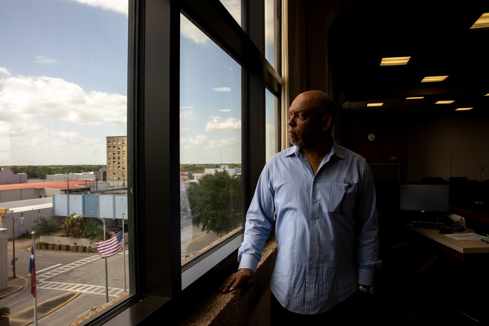 A man in a blue button-down shirt stands in front of a large window.