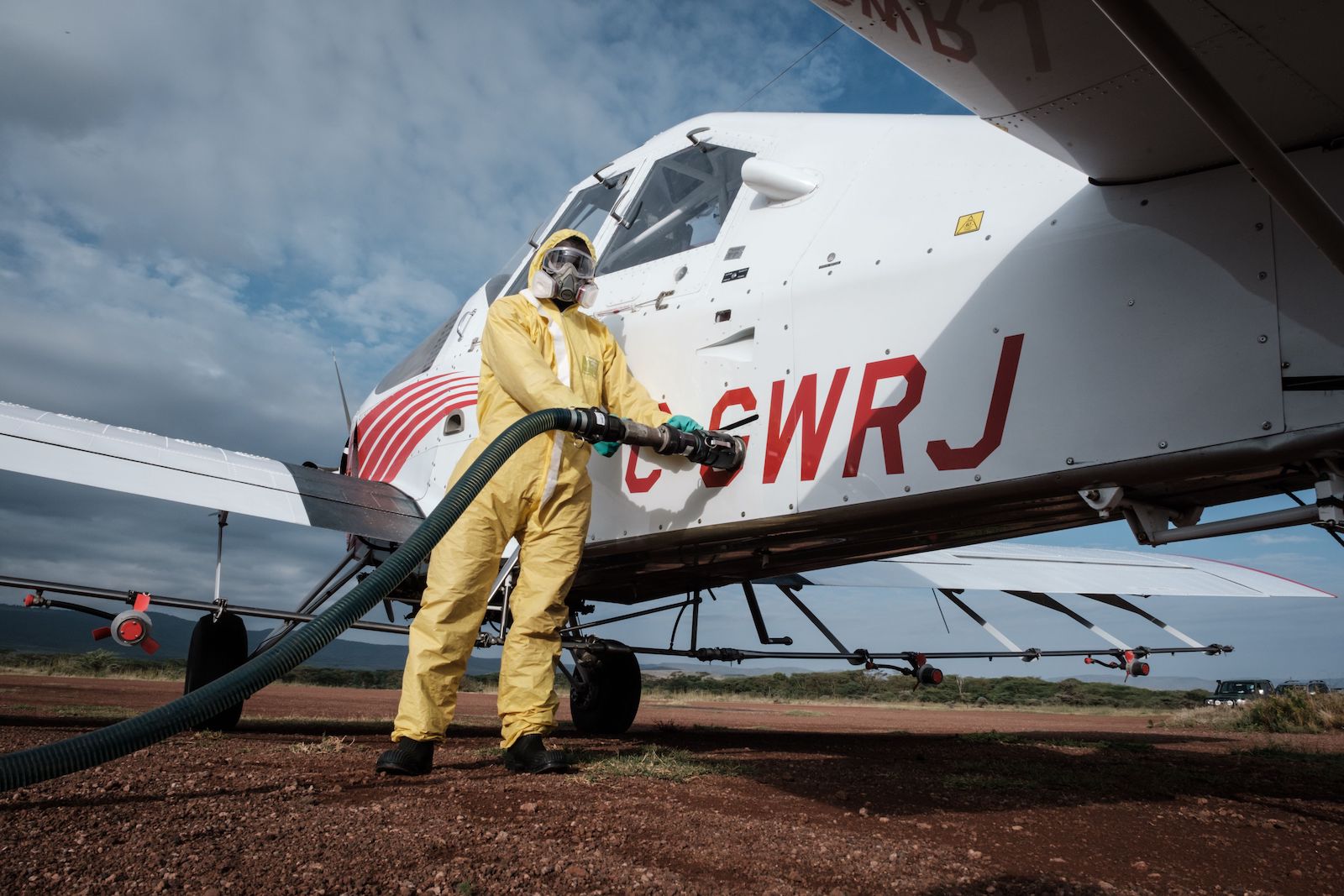 a person in a full-body yellow suit holds a black hose connected to a plane