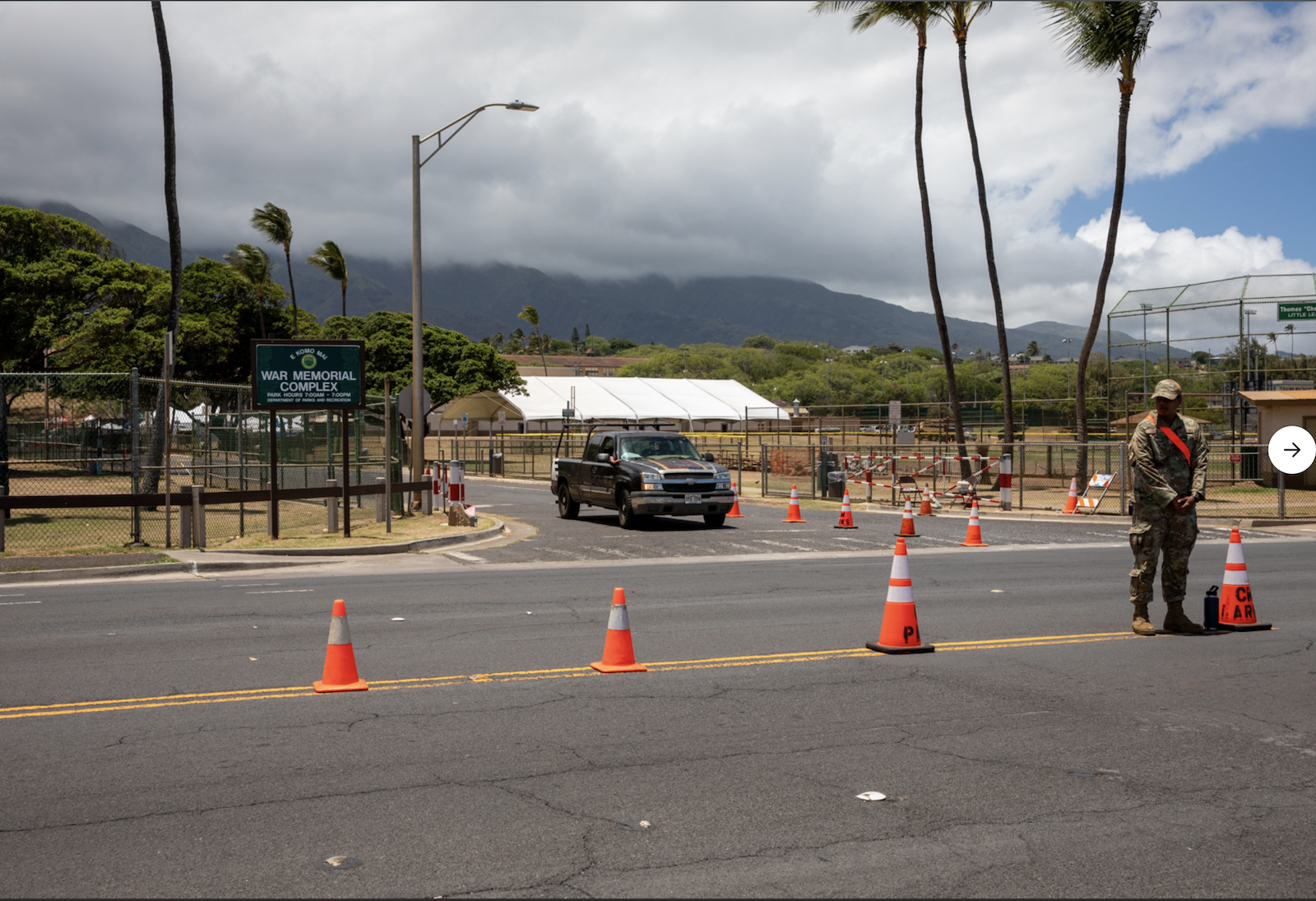 a person in military uniform stands outside of a line of cones near a sign that says war memorial complex