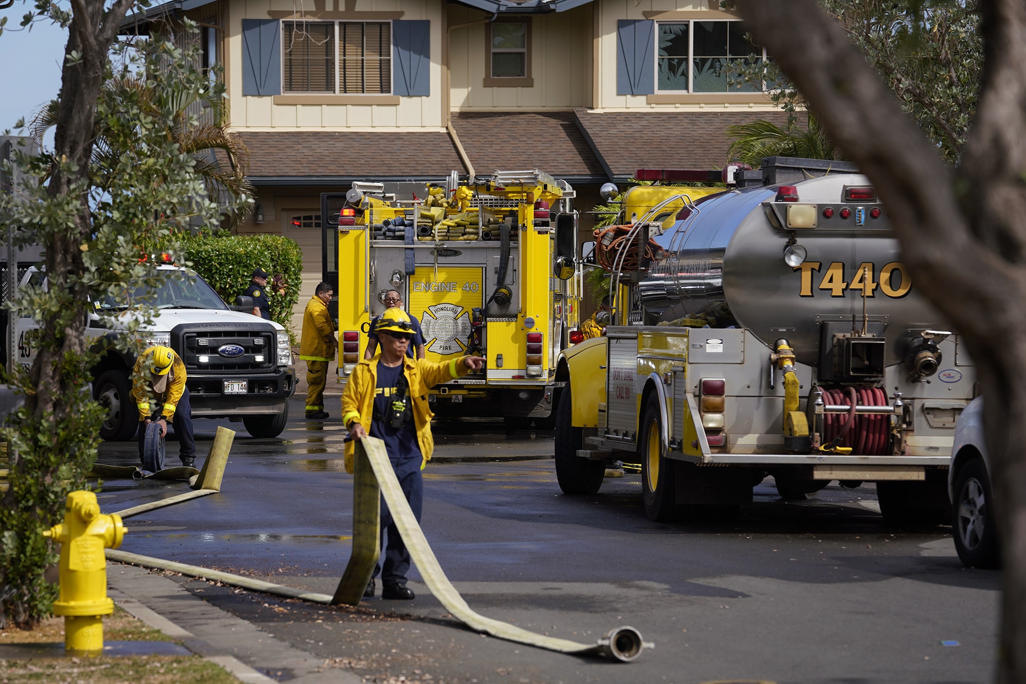 A firefighter outside of a home with a hose.