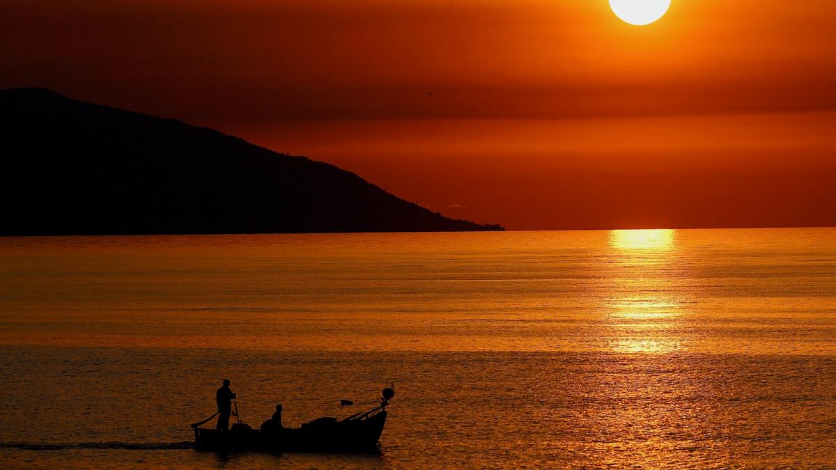 A small boat sails over the tranquil waters of the Black Sea at sunset.