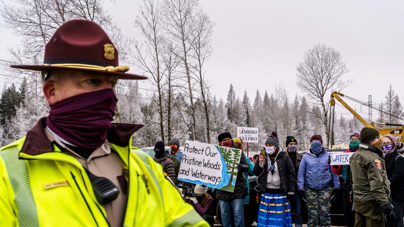 A policeman in a wide-brimmed hat stands in front of a group of protesters on a cloudy day.