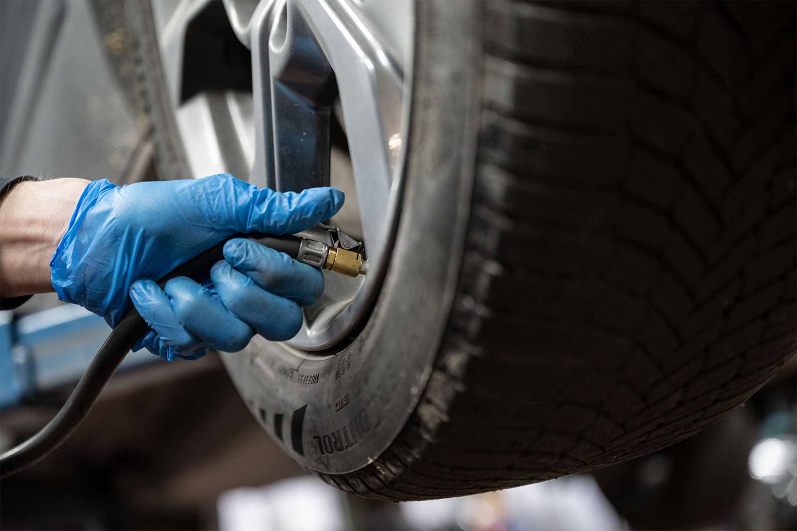 An employee at a workshop measures the air pressure of the tires while servicing a Mazda MX-30 electric car.