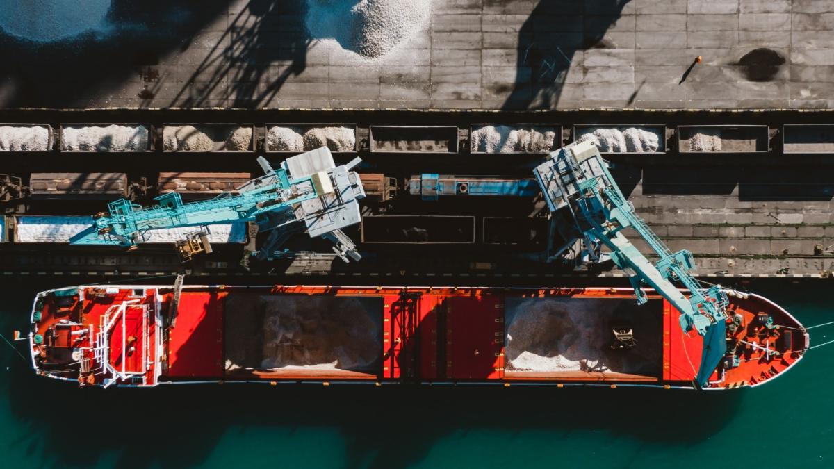 An aerial shot of a large ship with cranes unloading materials into train cars.