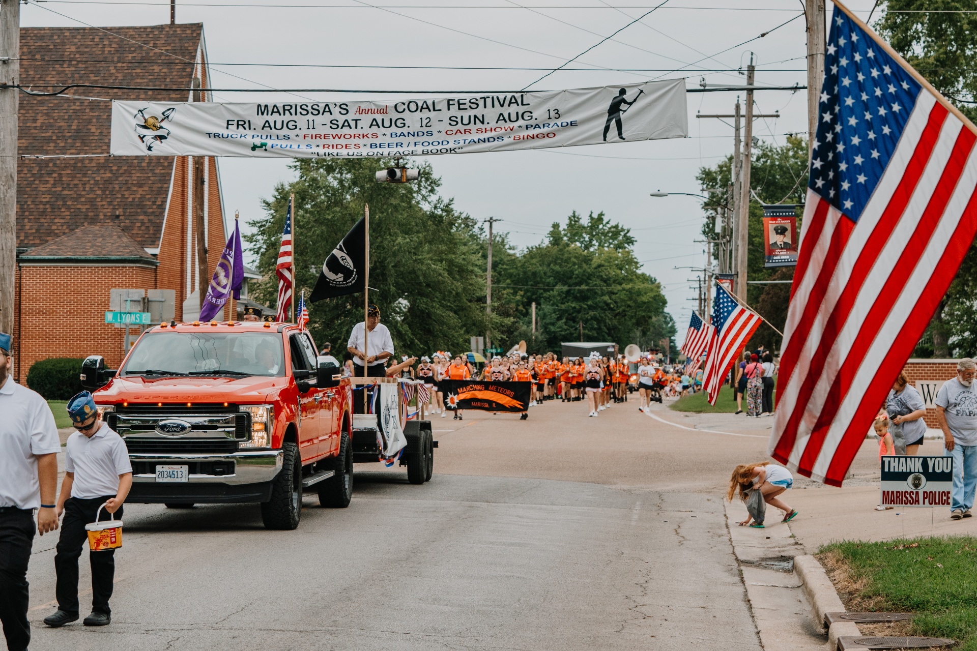 A red pickup truck is followed by a marching band dressed in orange uniforms