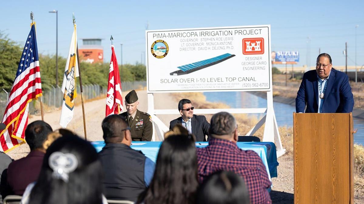 A man stands at a podium next to a sign in front of a group of people.