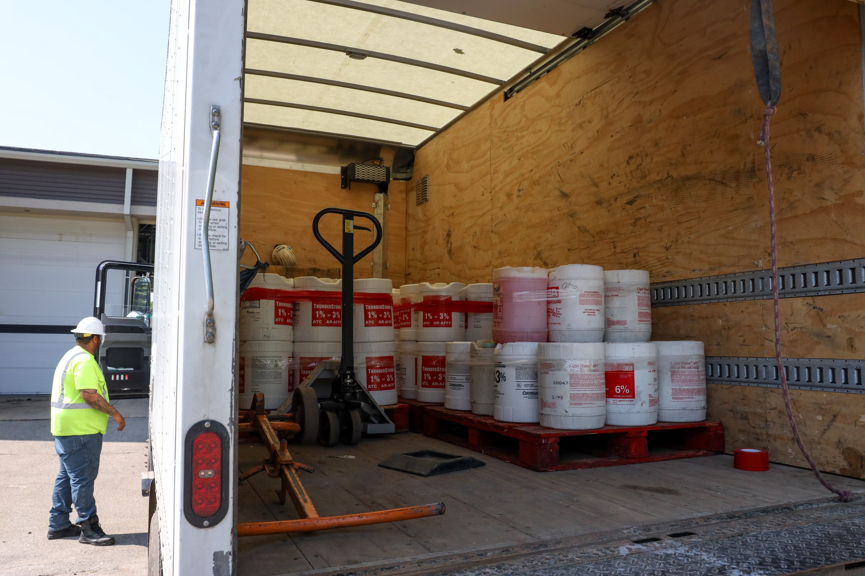 A man in a hard hat looks at a truck, which is open and holds large white containers.