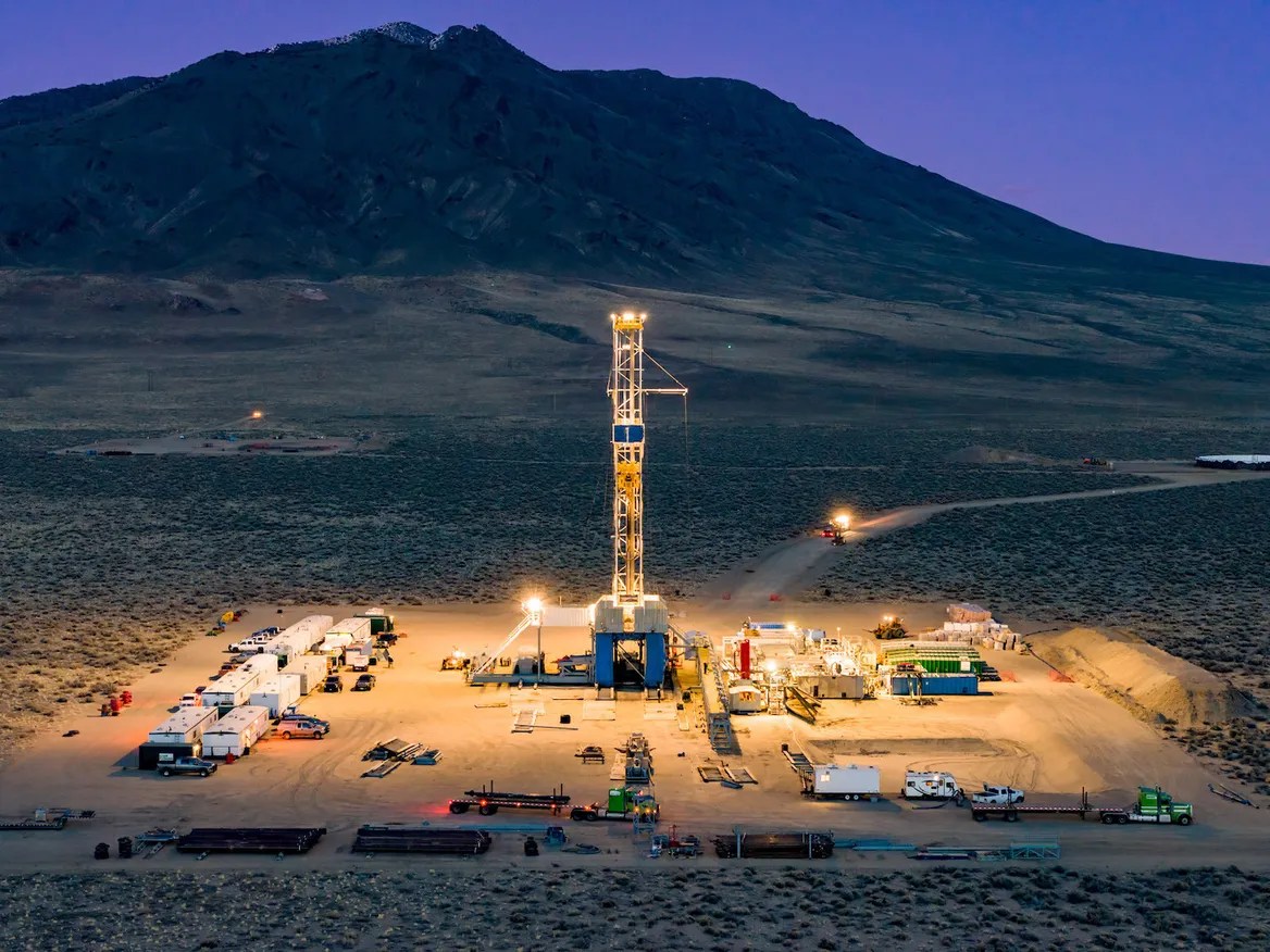 A mountain at night and an industrial facility lit up in front of it.