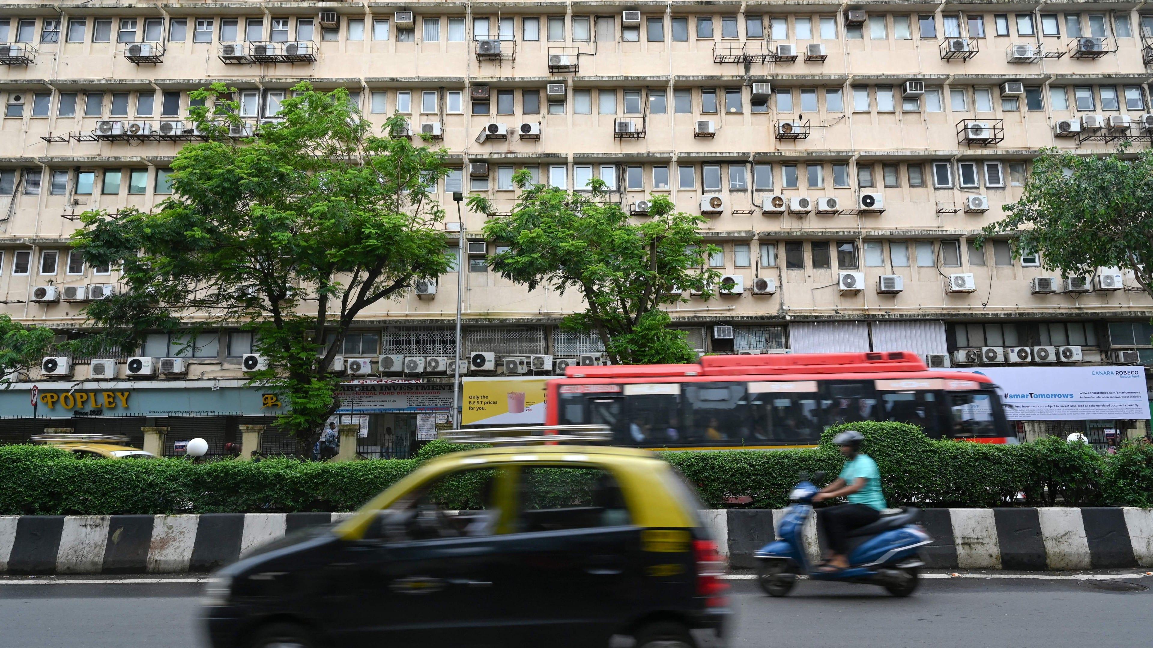 A taxi and motorcycle speed by an apartment building with AC units.