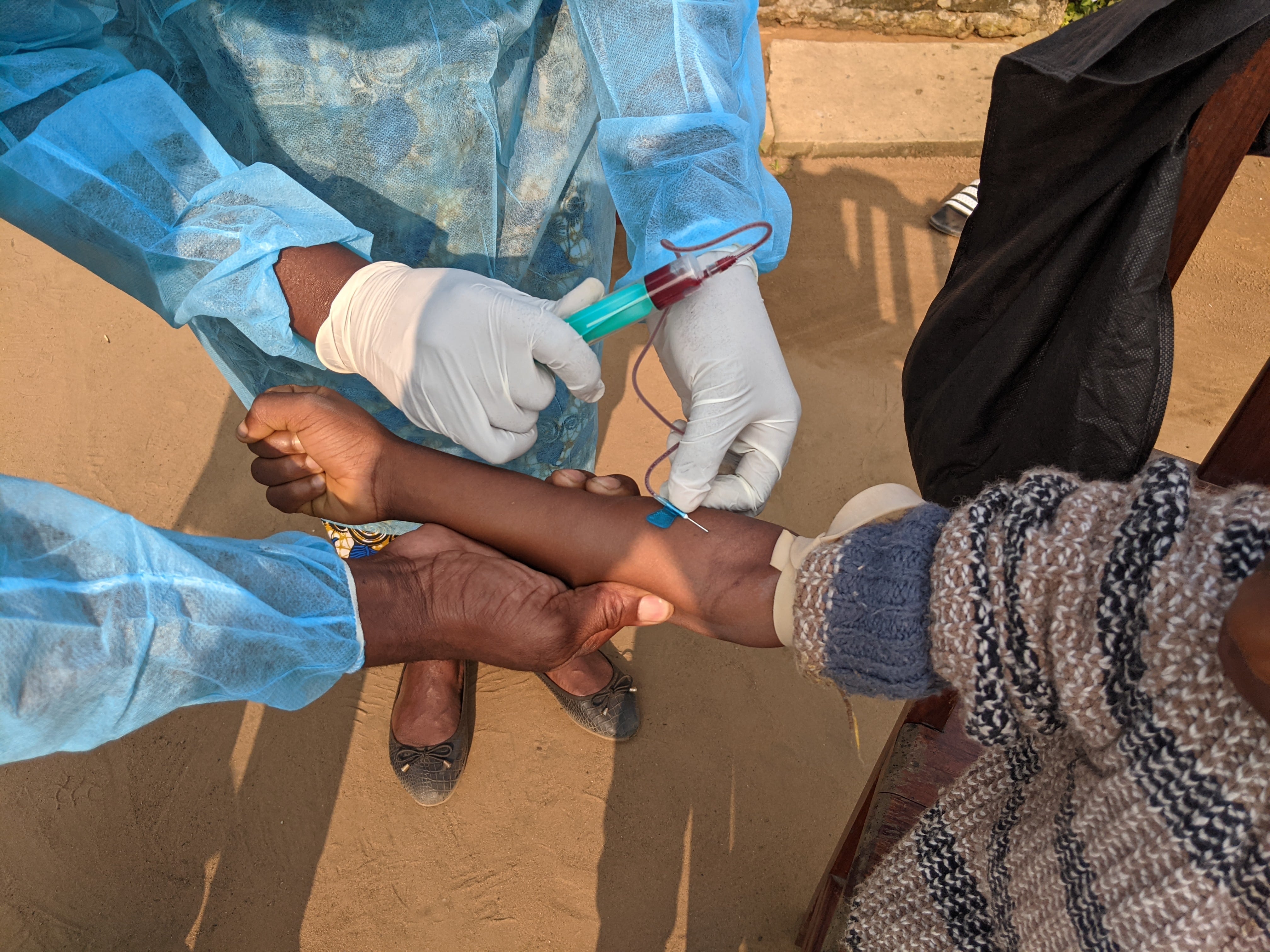 Two people wearing scrubs and latex gloves hold a woman's arm as they take her blood.