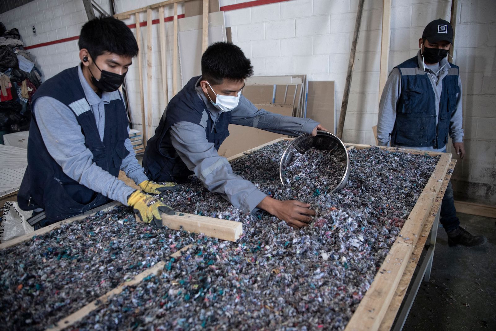 three men in vests sort through macerated textiles