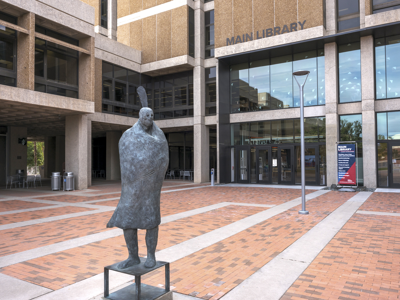 A statue of a person with a blanket and feather stands outside a building labeled main library