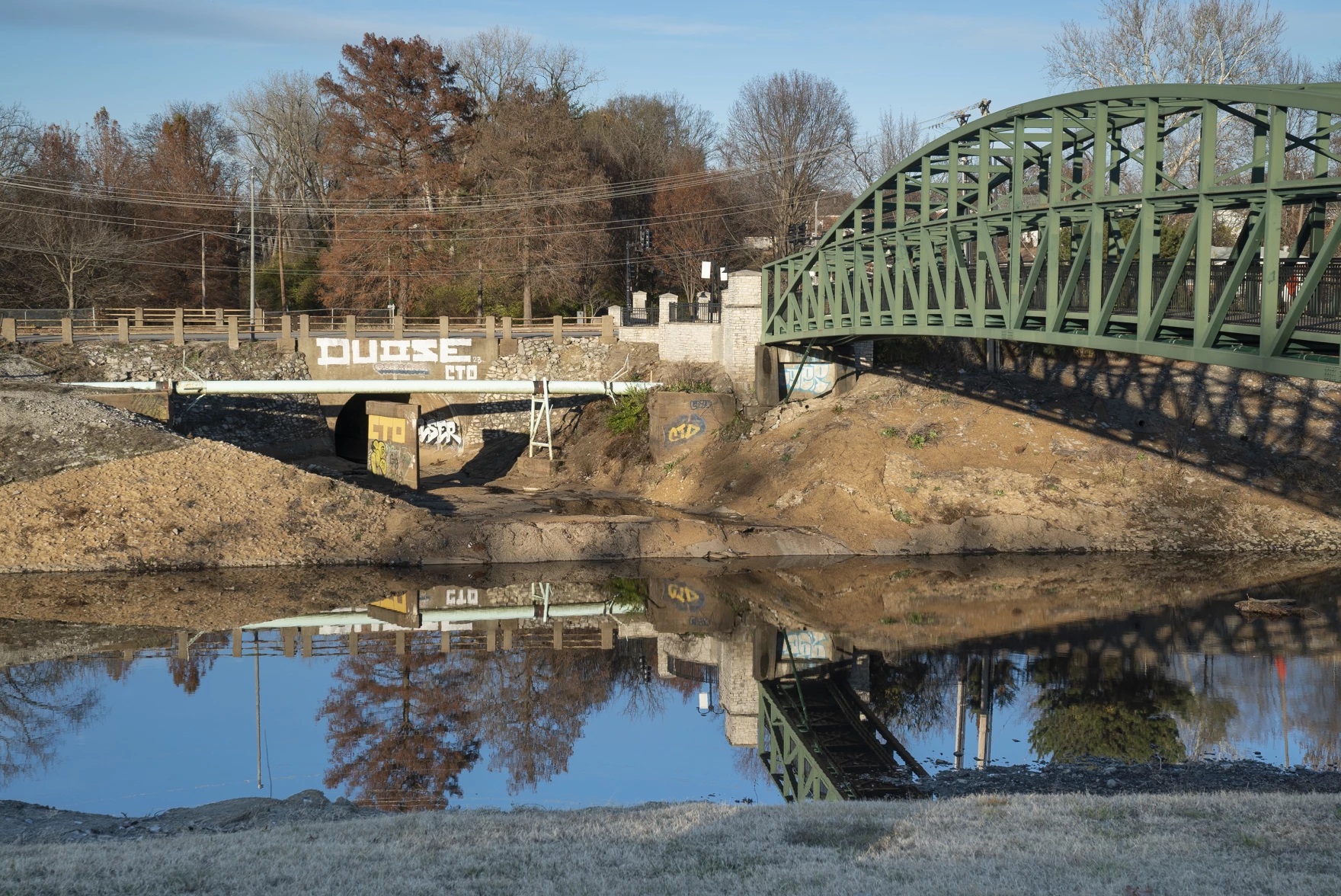 A green bridge runs over a dark creek.