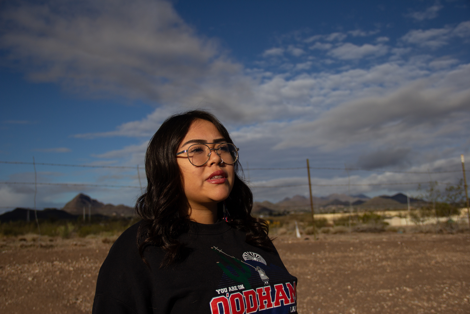 a woman looks to the right while standing in a desert community