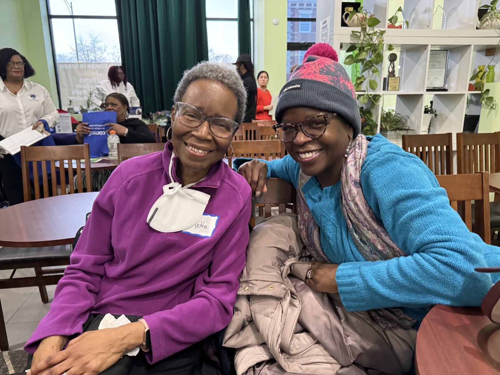 two women in sweaters sit and pose for a photo smiling