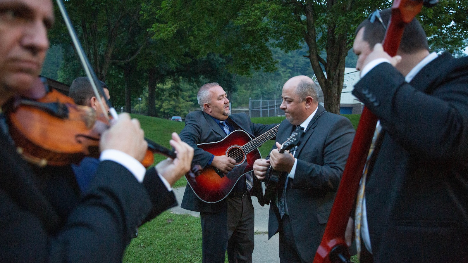 A bluegrass band of five men playing musical instruments warms up before a music festival in Hyden, Kentucky.