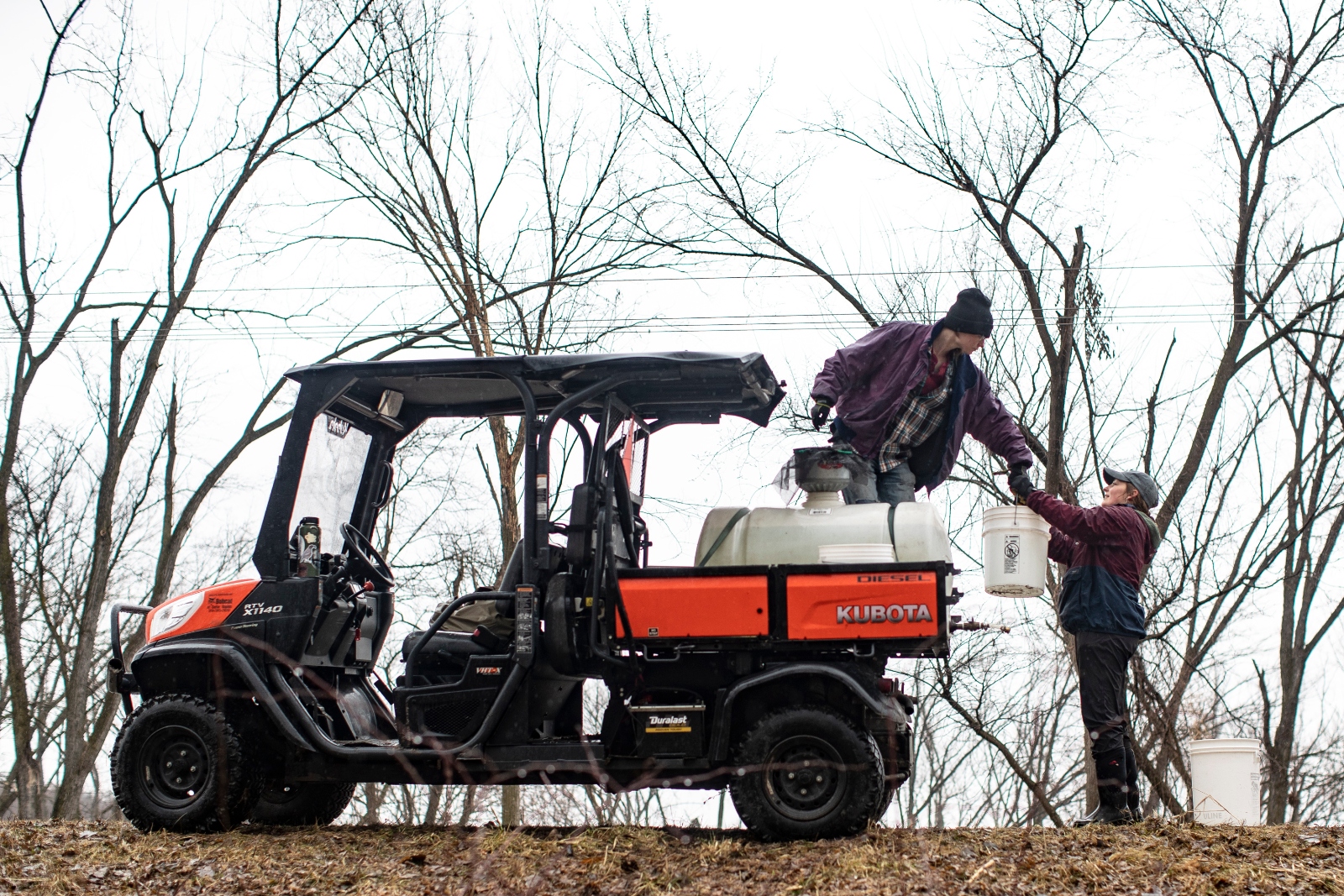 A person in a beanie and jacket stands in the back of a cart and hands a man