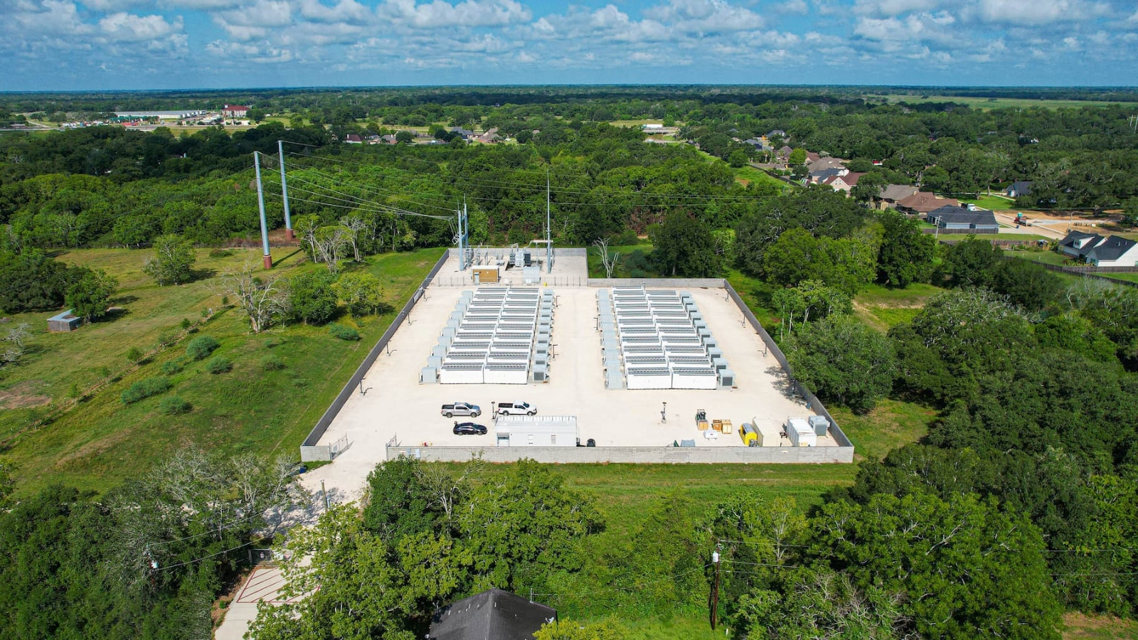 An. overhead shot of a green field and trees with a concerte platform in the middle with large black panels lined up on top.