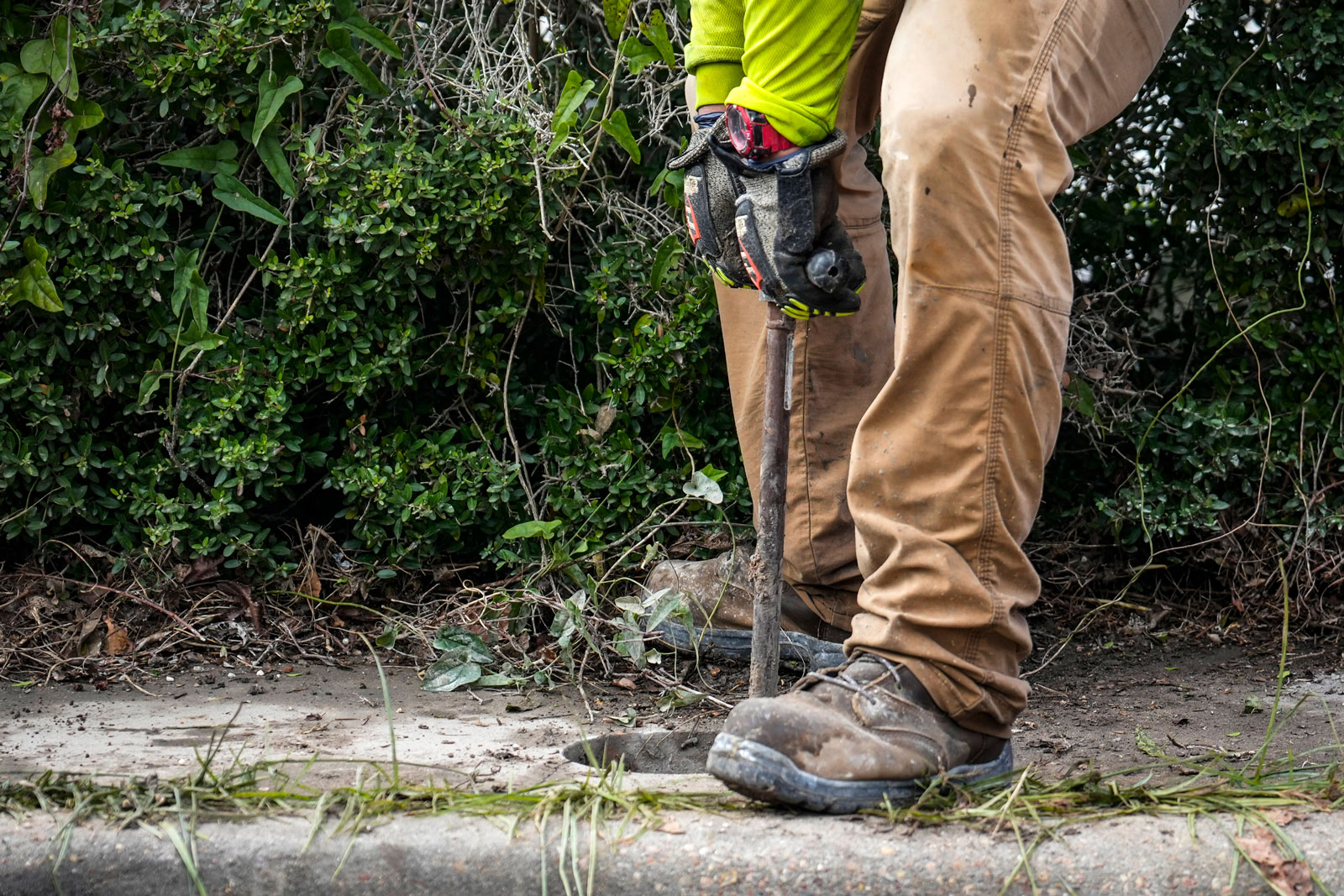 A contractor drops a well pipe into a sidewalk hole between their feet