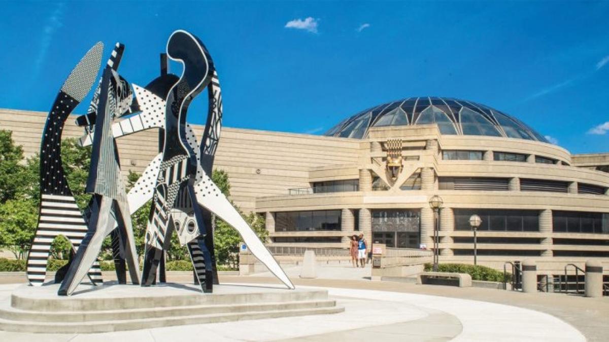 An exterior of a building with a large dome. A sculpture stands in the foreground.