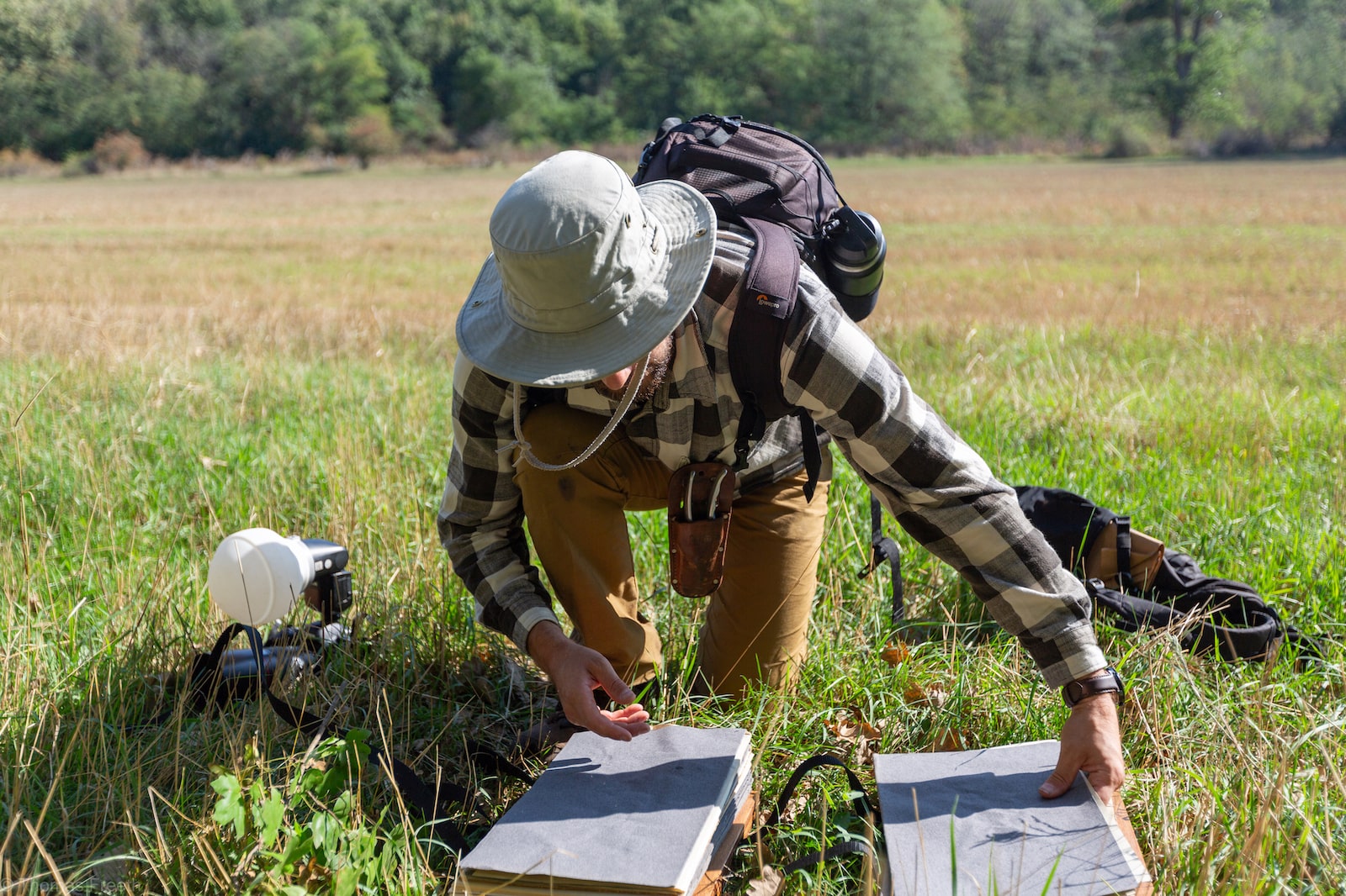 A man in a sun hat bends over a box in the middle of a field