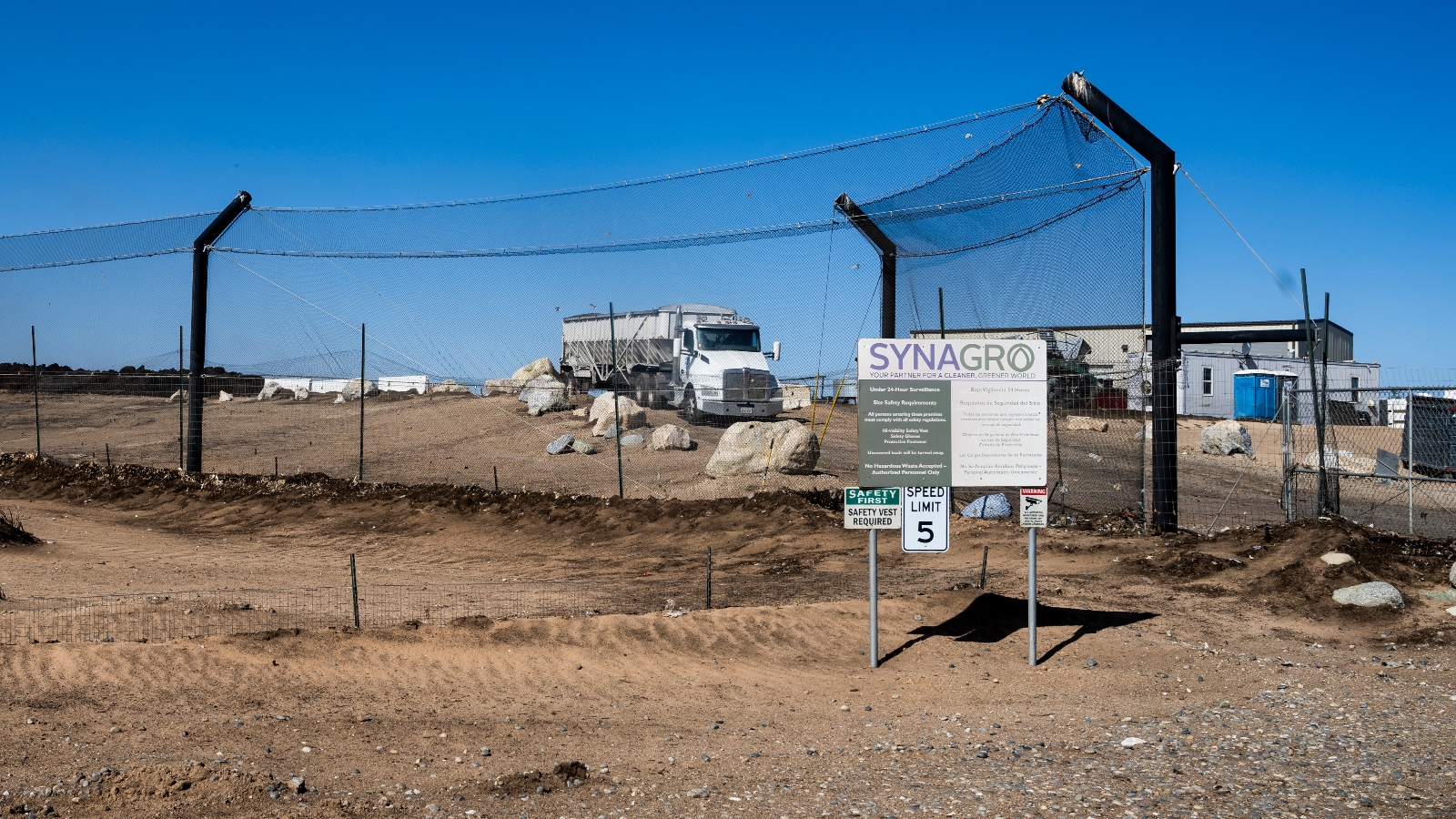 A sign says Synagro in front of an outdoor fenced area that contains a white semi truck