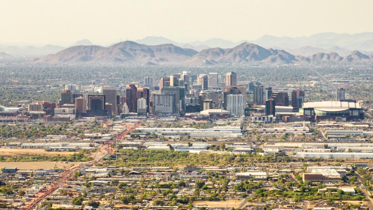 An aerial view of a city skyline surrounded by green areas and mountains in the background.