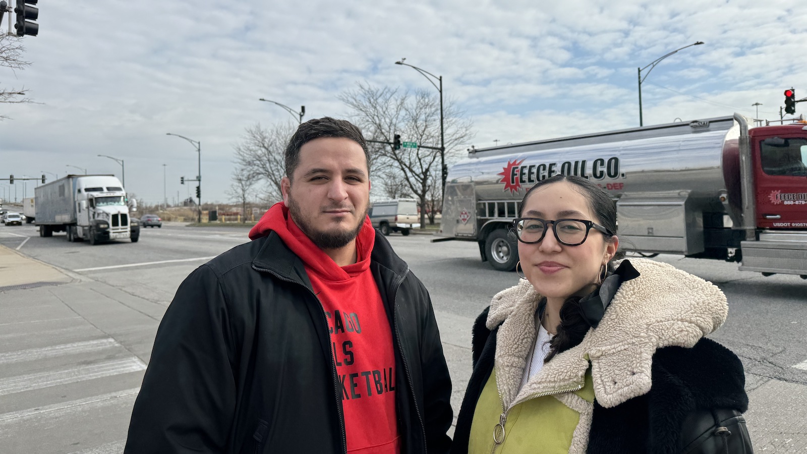 Aman and woman stand next to a road intersection with a truck in the background.