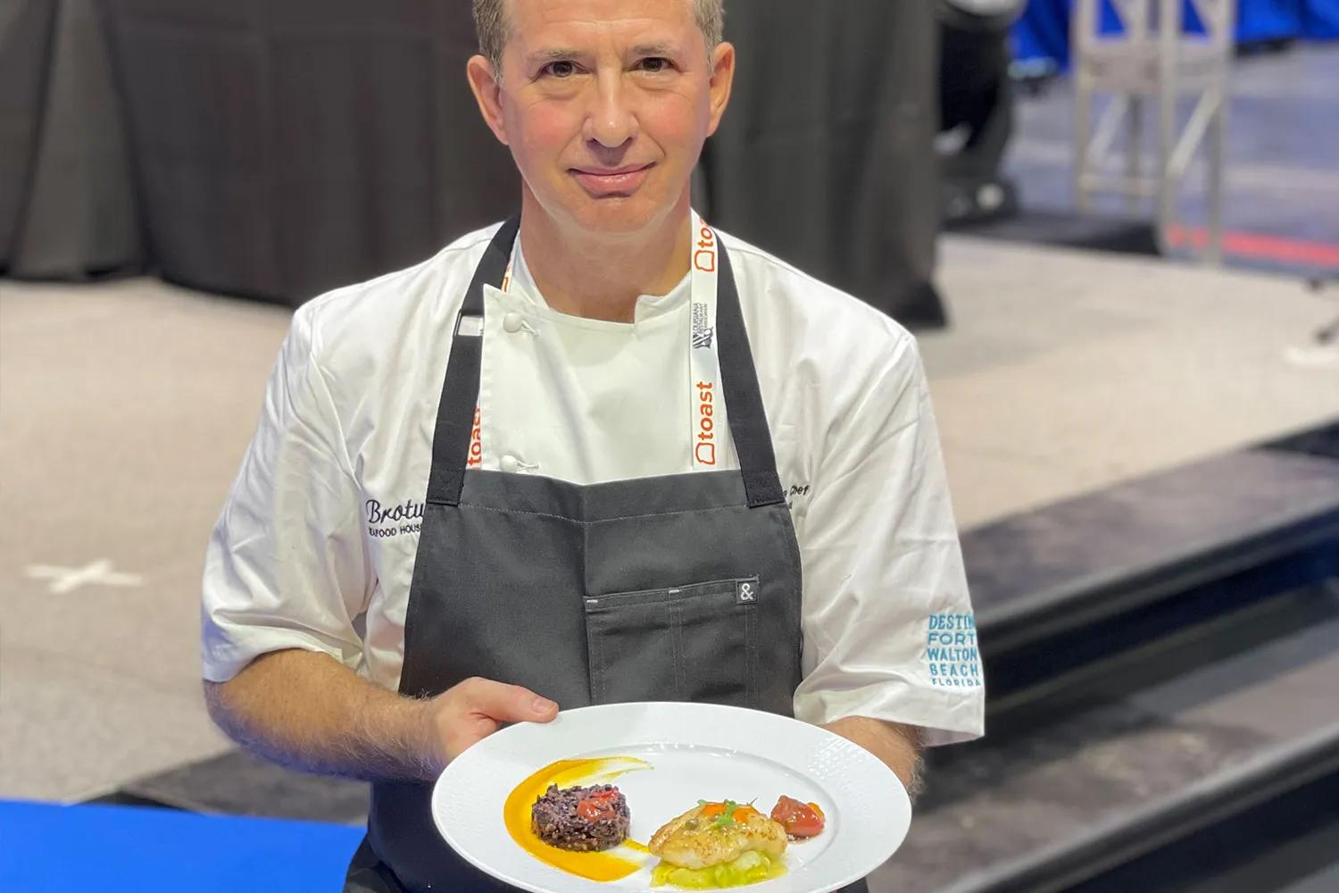 Chef wearing apron holds plate of pan-seared lionfish and forbidden rice