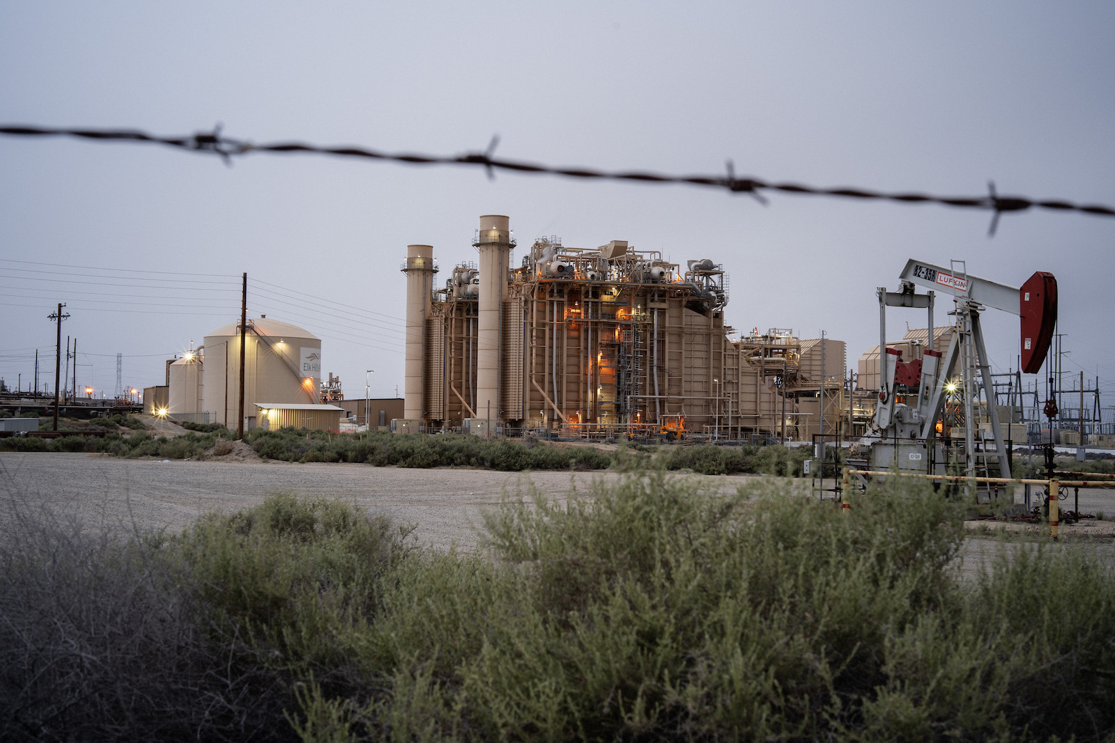 Barbed wire stretches across the view of a power plant and pumjack