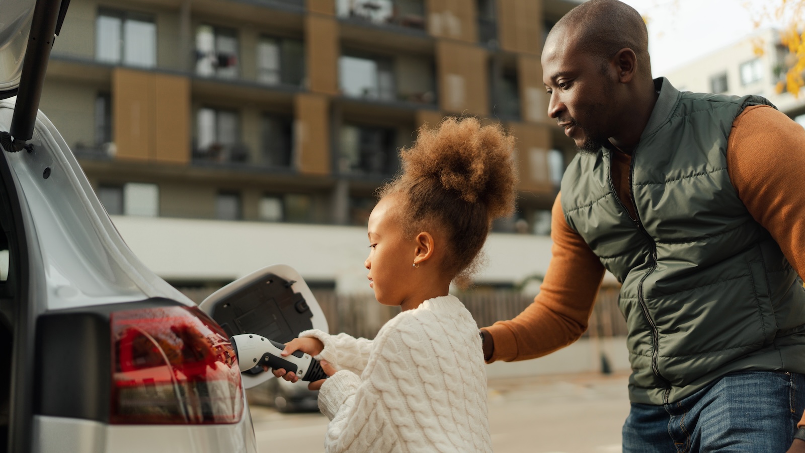 A father and his young daughter plug in their electric vehicle outside their home.