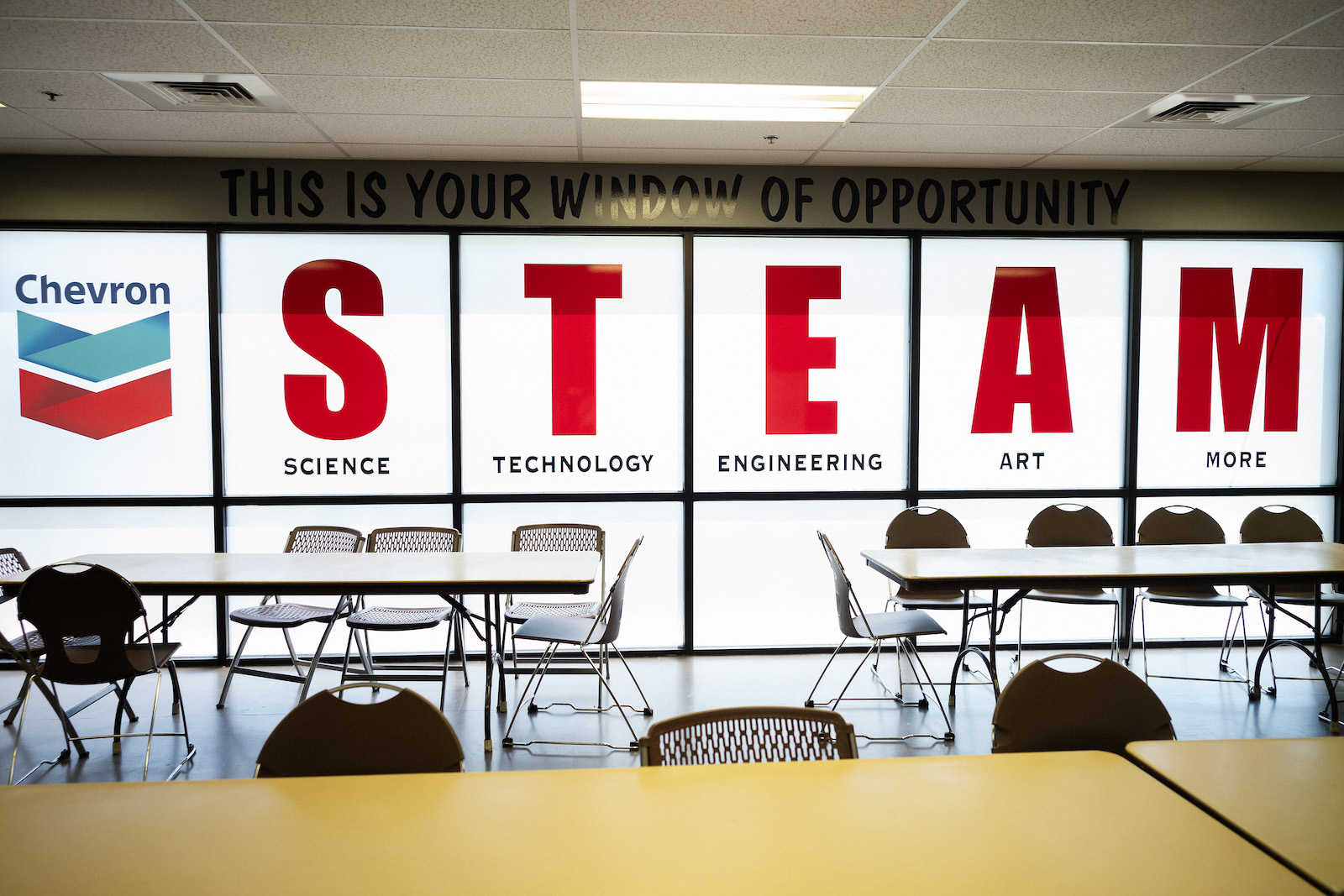 A window that say STEAM with a Chevron logo inside a conference-style room