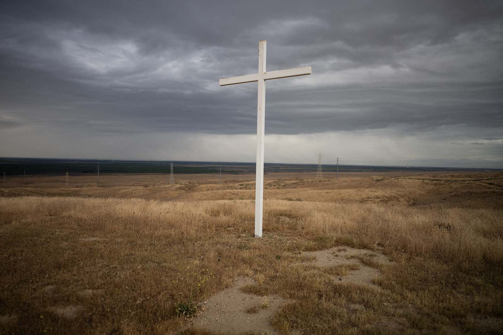 A large white cross on a field with pumpjacks