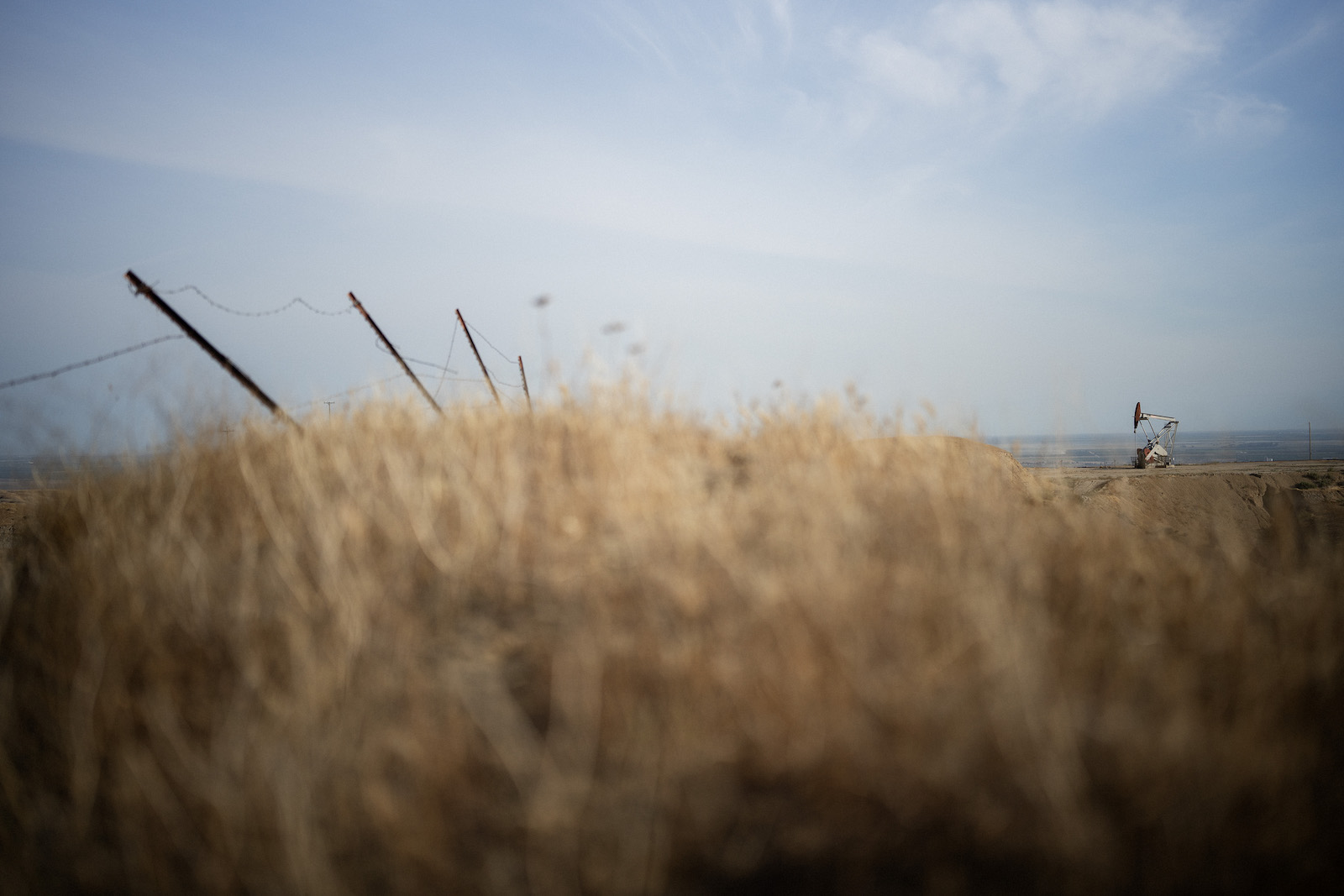 A fence teeters over a golden field near a pumpjack